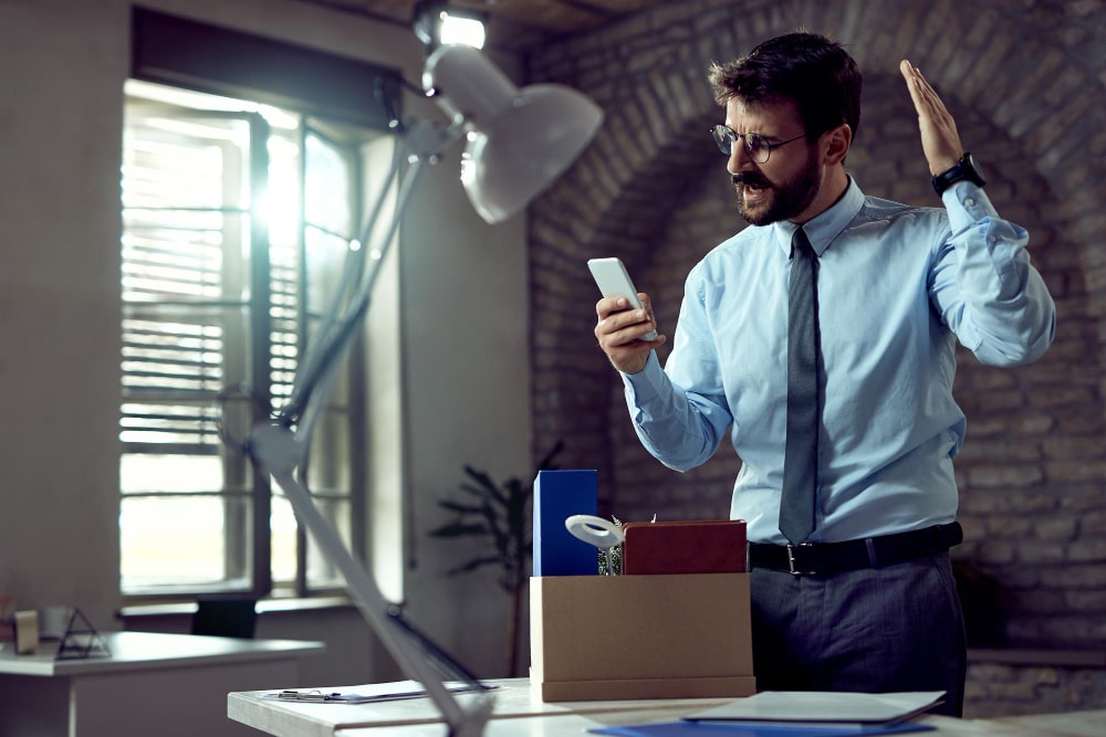 young businessman reading text message cell phone while feeling angry about losing his job office min